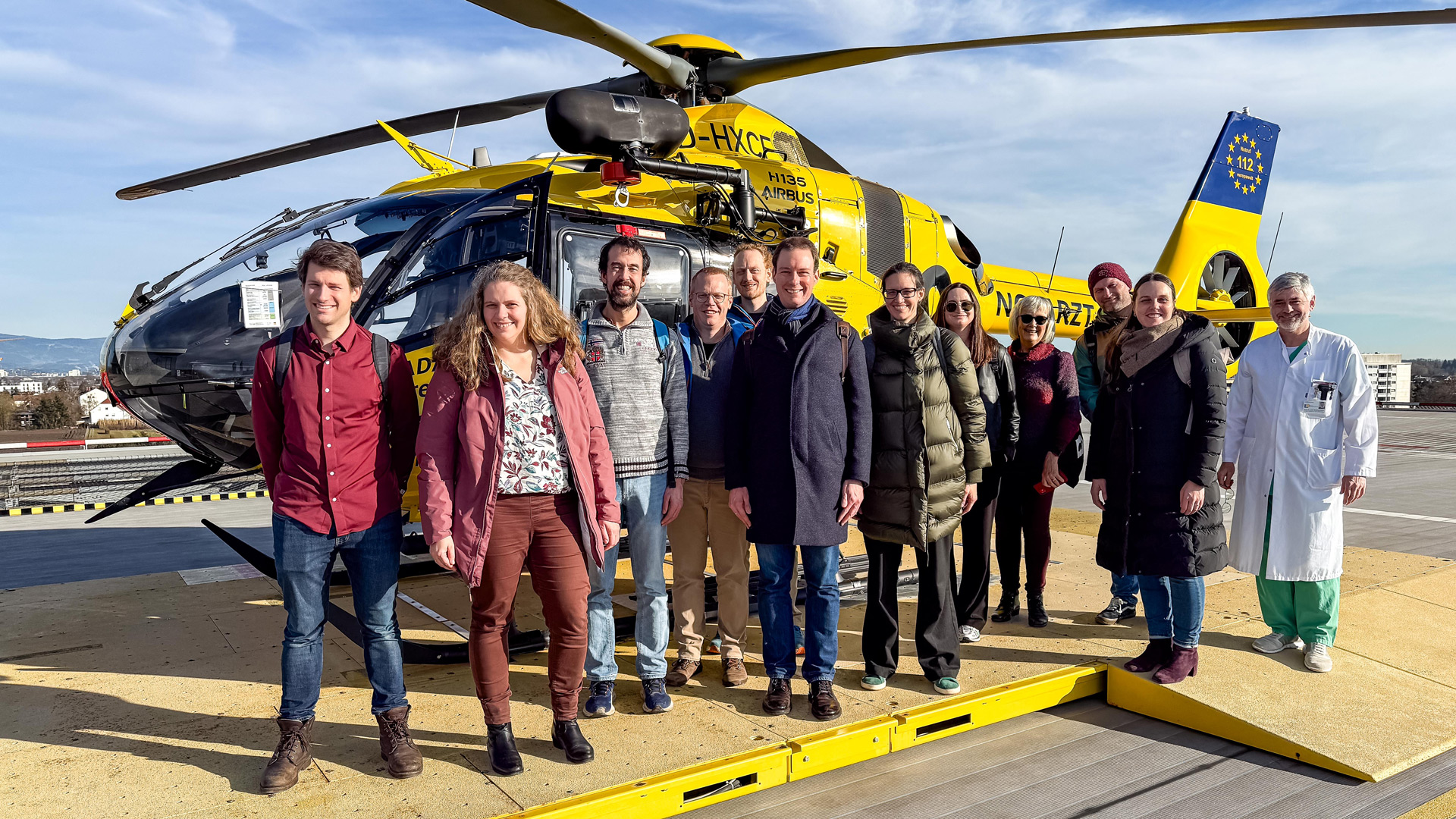 A group of people standing in front of a yellow helicopter on top of the Straubing hospital